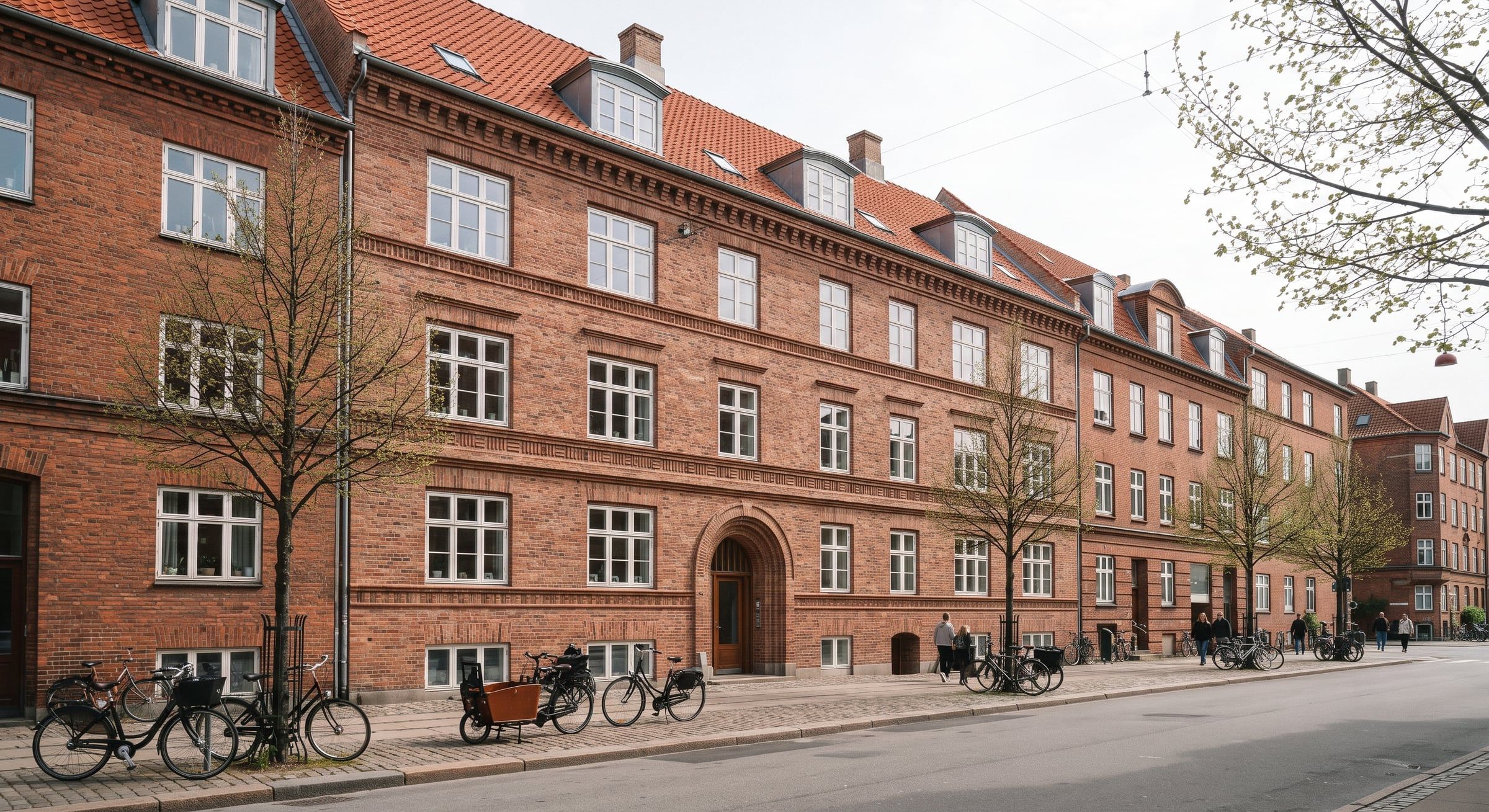 Karré i røde sten med sprossede vinduer langs en bygade med cykler.